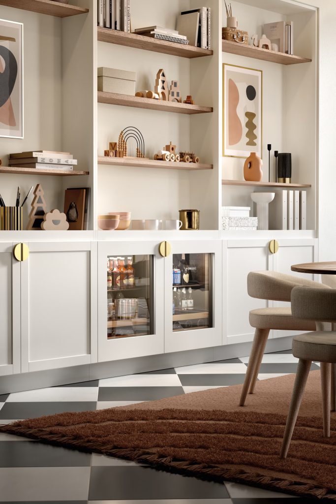 Under-counter beverage cooler repair on a dual glass-door unit built into a white cabinetry wall beside open shelves with art and books.