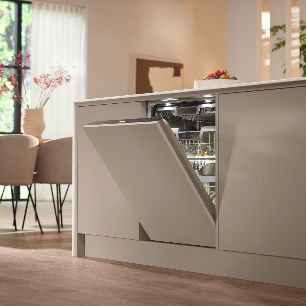 Integrated dishwasher repair on a panel-ready Miele unit with its door tilted open inside a beige kitchen island near the dining area.